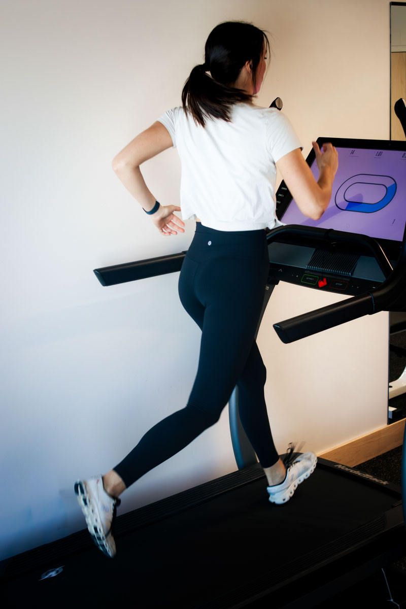 Woman wearing black leggins and white top running on treadmill 